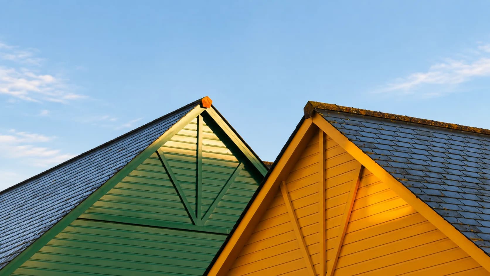 Two gable ends, one green and one yellow, under slate roofs at sunset