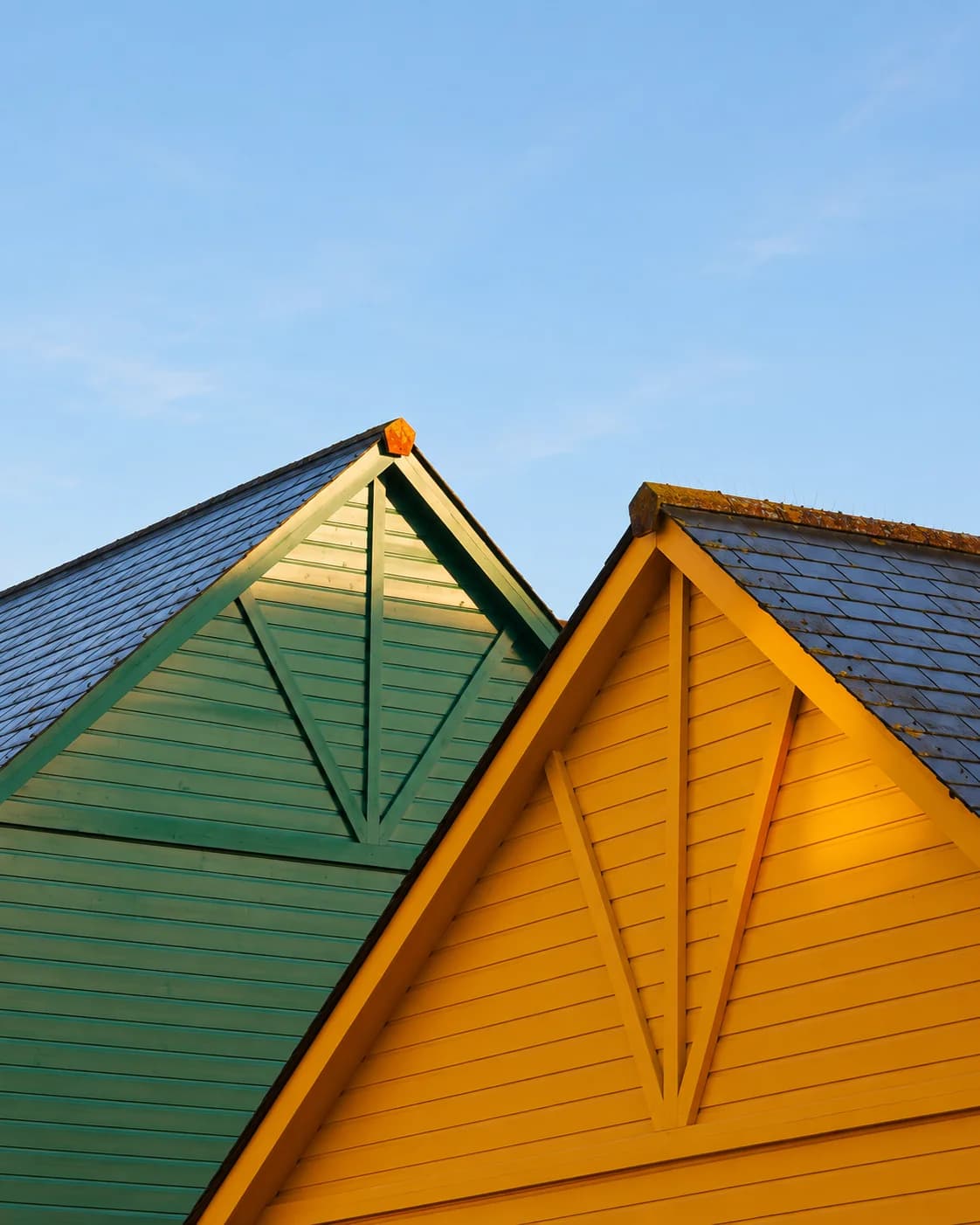 Two gable ends, one green and one yellow, under slate roofs at sunset