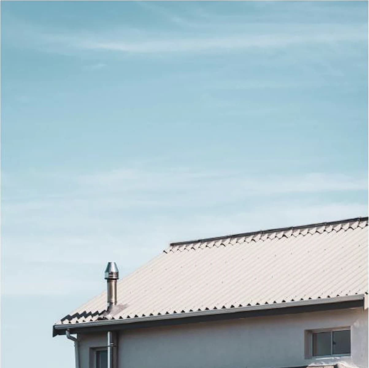 Cream tile-profile metal roof against a pale sky